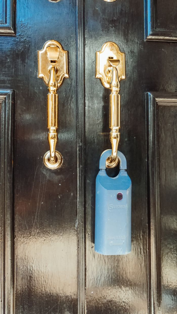 services-01 Close-up of a sleek black door with shiny brass handles and a blue lockbox, ideal for real estate security concepts.