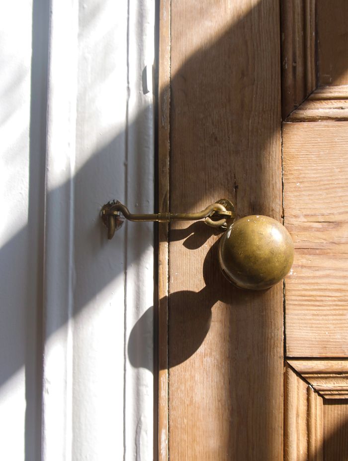 services-01 A detailed image of a brass door knob with a latch, casting shadows on a wooden door.